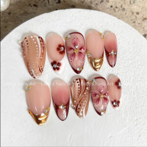 Elegant burgundy press on nails with 3D pink flowers, gold chrome accents, and water droplets on white surface